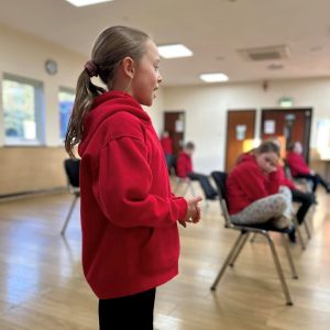 Young girl wearing a red hoodie practising oracy skills in a Little Voices lesson
